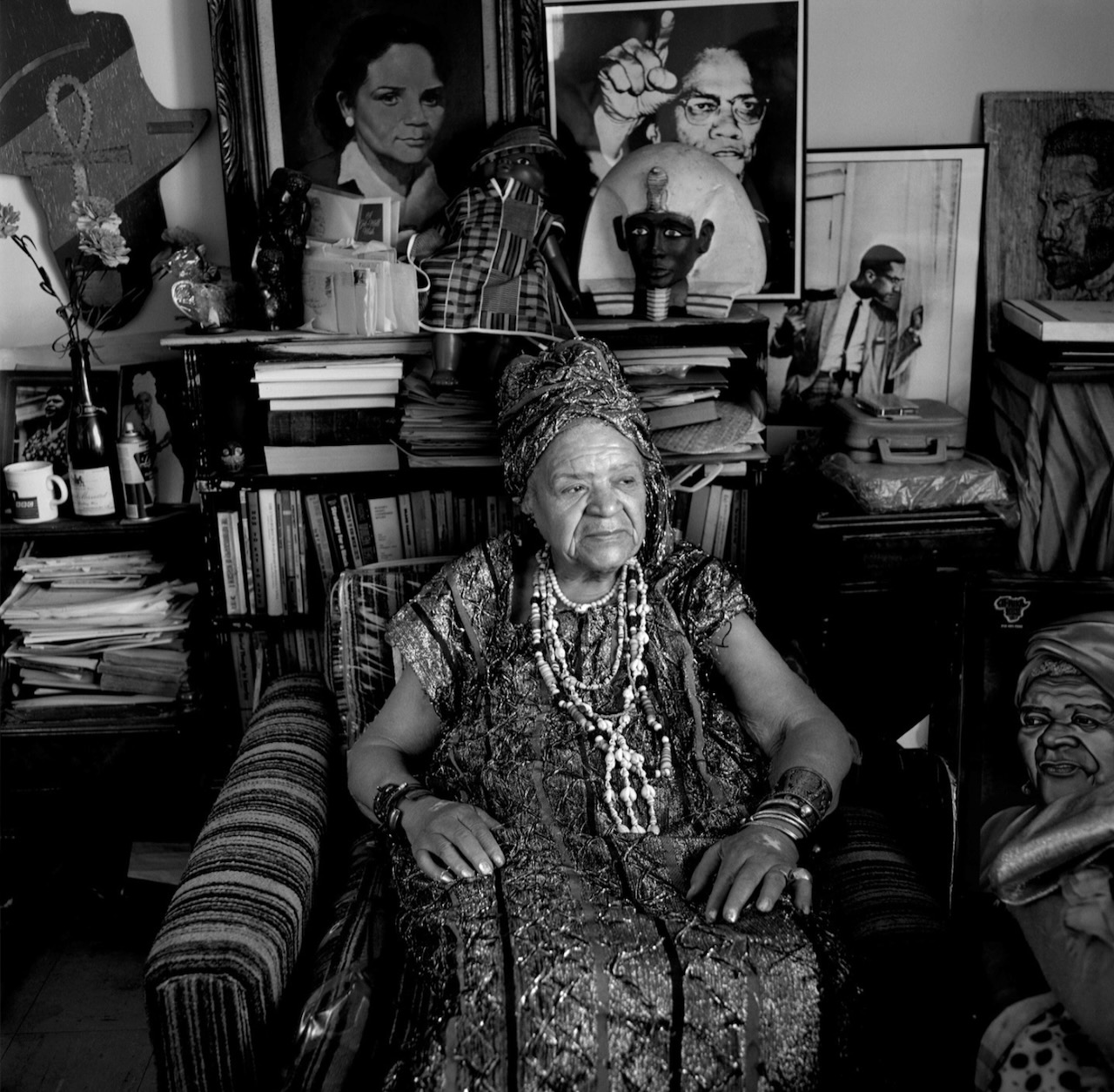 Portrait of an elder woman in African attire, surrounded by community art, portraits, and books